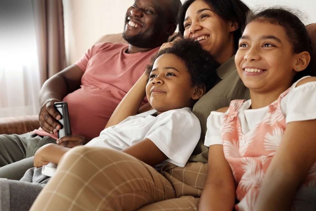 A Evolução do Direito de Família: Família sorridente assistindo televisão juntos no sofá, simbolizando a união e a proteção legal das famílias no Brasil.
