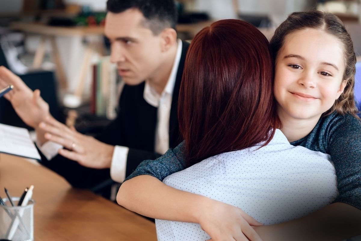 Nova Lei Guarda Compartilhada Ganha Força no Brasil: uma criança sorridente abraça uma mulher de cabelos ruivos, enquanto um homem de terno gesticula ativamente em primeiro plano, ilustrando uma discussão ou consulta.