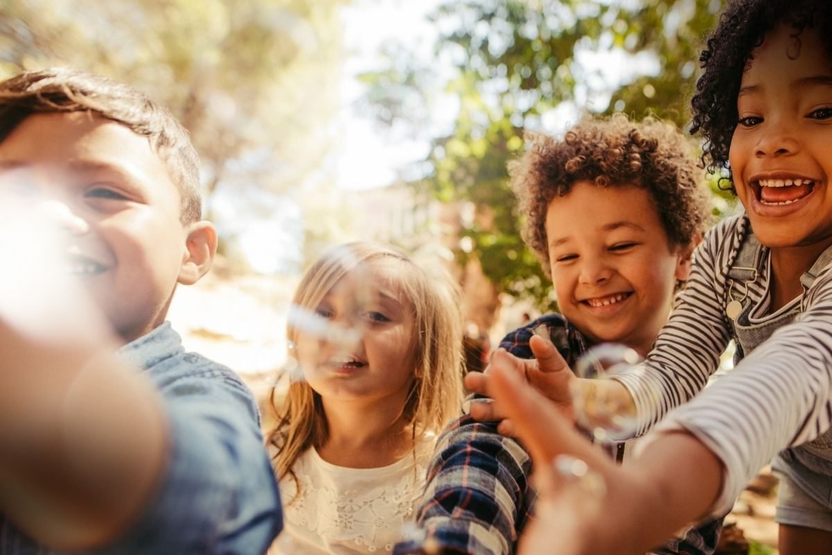 Parentalidade Positiva - grupo diversificado de crianças sorridentes brincando ao ar livre, capturando a alegria e o direito ao brincar em um ambiente ensolarado e natural.