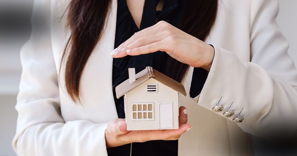 A partilha de imóvel financiado em processos de separação representada por mãos femininas protegendo uma maquete de casa.