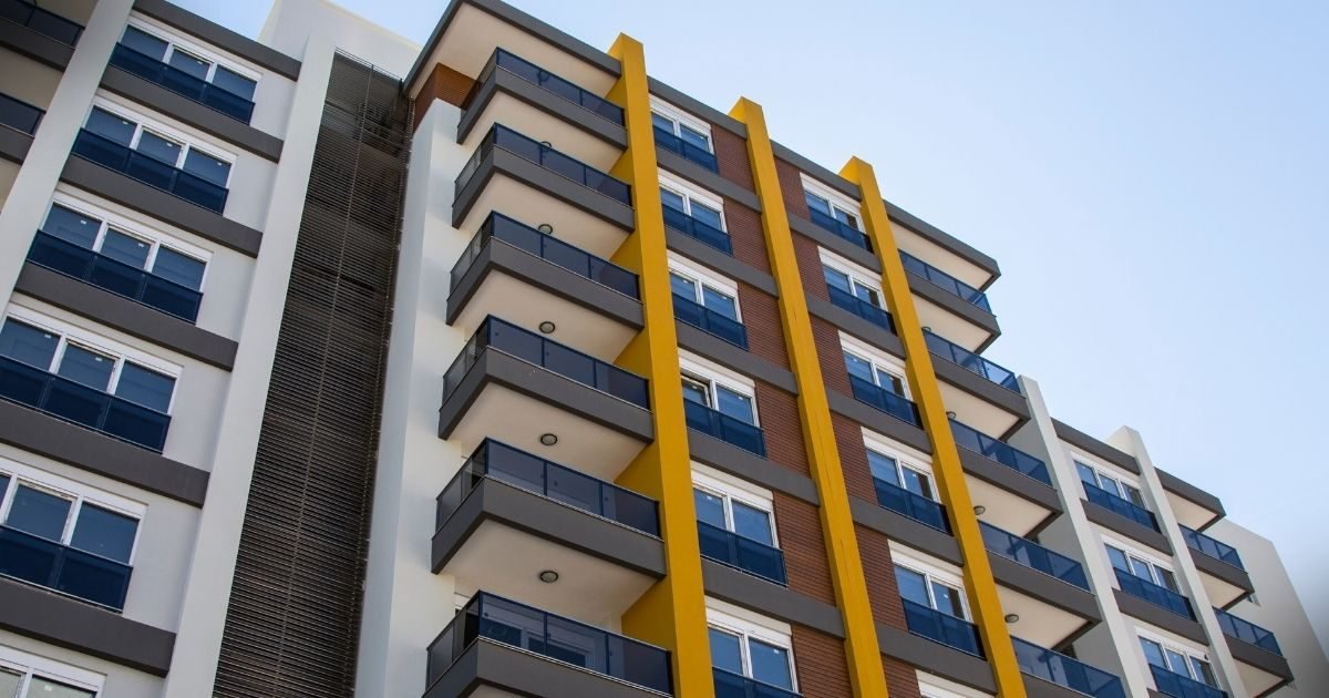Decisão do STJ: vista de ângulo baixo de um moderno prédio residencial com varandas, detalhes em amarelo e marrom, simbolizando investimentos imobiliários e potenciais retornos financeiros.