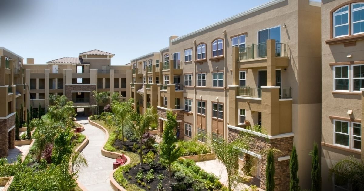 Herança e Dívidas Condominiais: vista aérea de um condomínio residencial moderno, exibindo fachadas bege com sacadas e janelas amplas, rodeadas por jardins bem cuidados e caminhos sinuosos, exemplificando o contexto imobiliário para discussões jurídicas