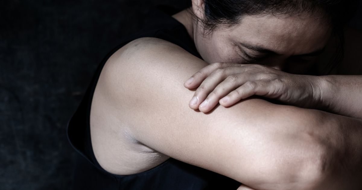 Medida Protetiva na Lei Maria da Penha: imagem de uma mulher abraçando o próprio ombro, transmitindo uma sensação de proteção, com fundo escuro para realçar o tema de segurança e apoio.